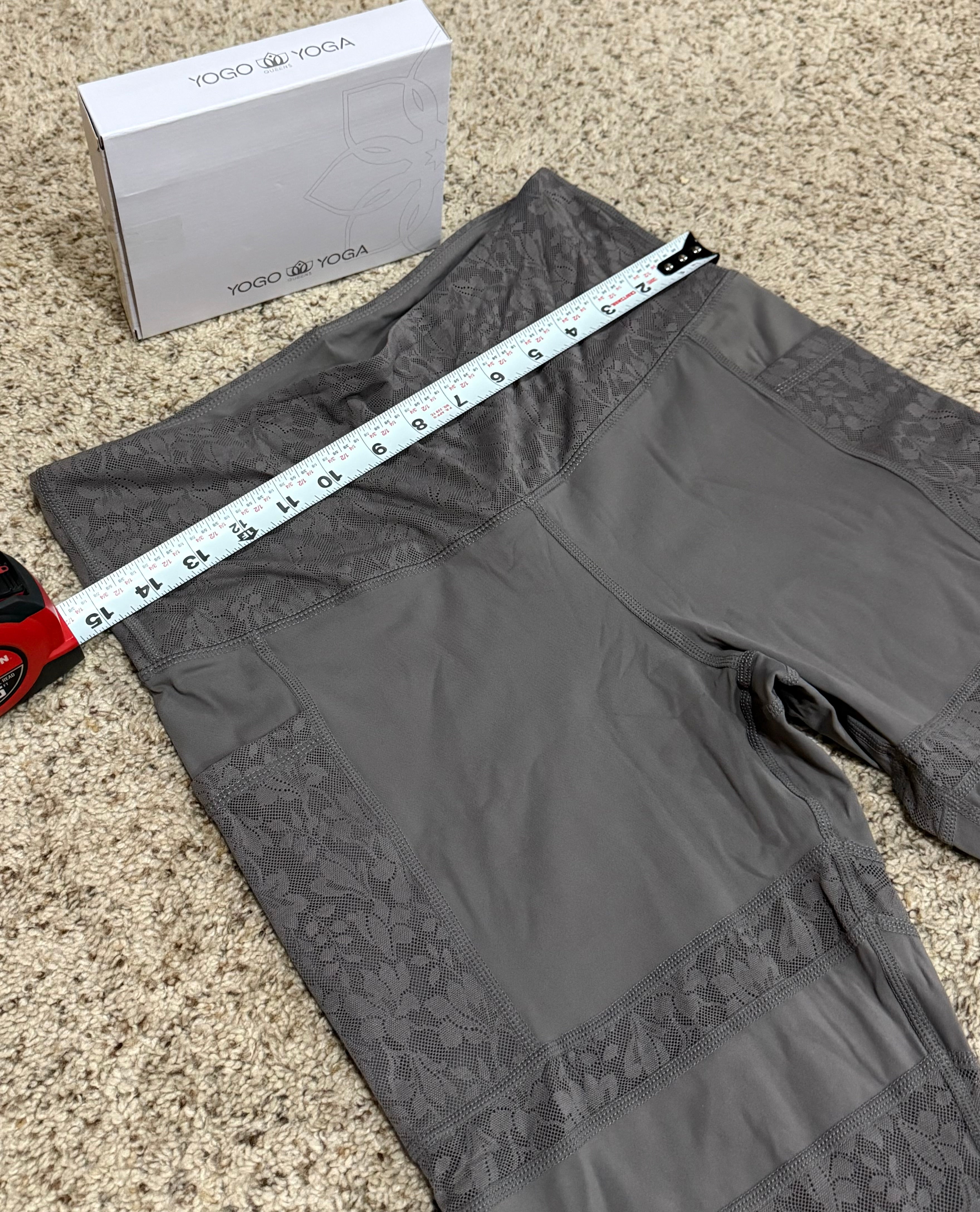 Gray leggings with lace trim being measured with a tape measure on a beige carpet.