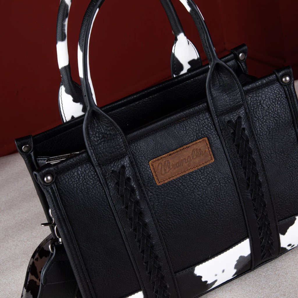 Front view: "Wrangler Cow Print Concealed Carry Tote Crossbody Bag Black — front view"
Interior/pocket view: "Wrangler Cow Print Concealed Carry Bag — interior concealed carry pocket detail"
Side/crossbody view: "Wrangler Black Cow Print Crossbody Bag — worn as crossbody style"