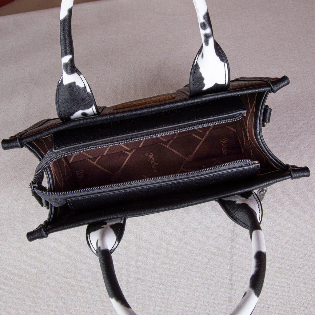 Front view: "Wrangler Cow Print Concealed Carry Tote Crossbody Bag Black — front view"
Interior/pocket view: "Wrangler Cow Print Concealed Carry Bag — interior concealed carry pocket detail"
Side/crossbody view: "Wrangler Black Cow Print Crossbody Bag — worn as crossbody style"